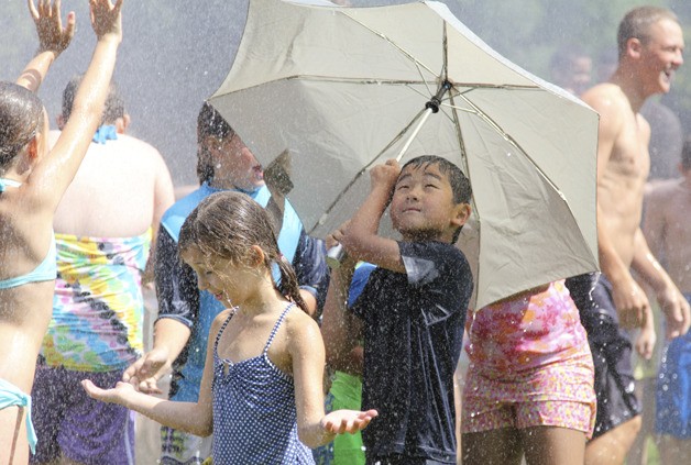 A boy holds up an umbrella to find some reprieve from the spray of a fireman’s hose on Splash Day in Issaquah.