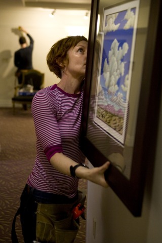 Kelly Staton hangs one of the last paintings to go up ahead of tonight’s University House art exhibition opening.