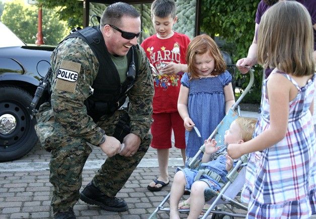 Issaquah police officer Nathan Lee greets children outside city hall with police badge stickers for National Night Out. A few hundred people visited city hall to visit with police from various agencies Aug. 2.