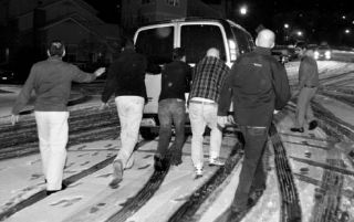 Bystanders help a church van negotiate its way up Northeast Park Drive last Saturday. The road was quickly covered in snow by a late-season