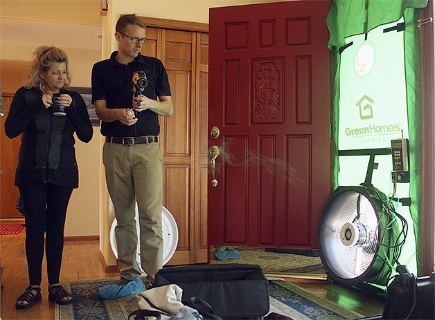 Sammamish homeowner Becky Henchman watches Washington Energy Services home auditor Cory Tobin use a smoke pen to show air leaks within the home. The fan hooked up to the front door simulates winds all around the house to demonstrate how airtight the home is. Tobin