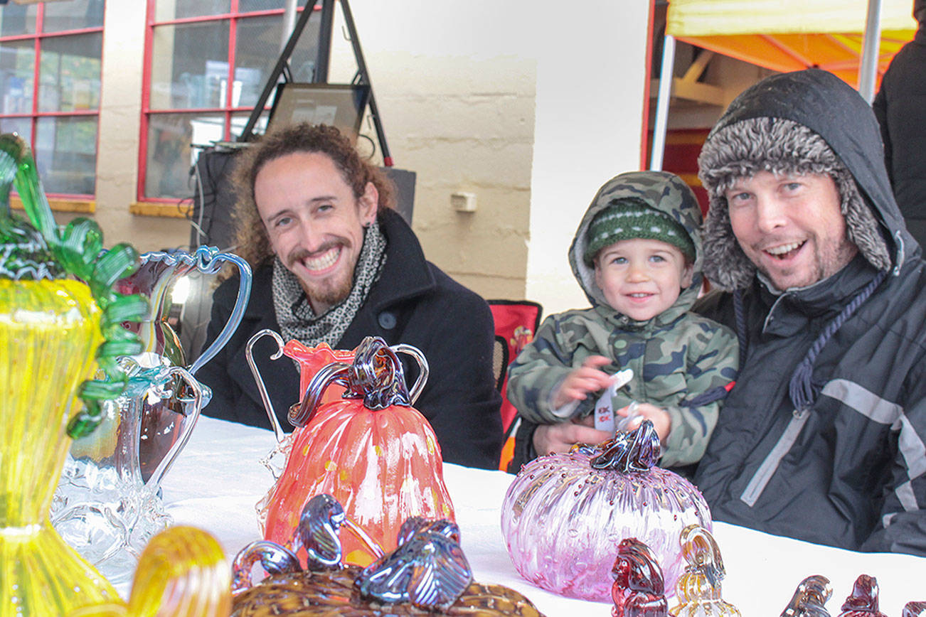 Brockman Guinee, John Ezell and John Jr. at the Art by Fire table during the Issaquah Goes Apples fair Oct. 19, selling glass blown pumpkins and apples. Natalie DeFord/Staff photo