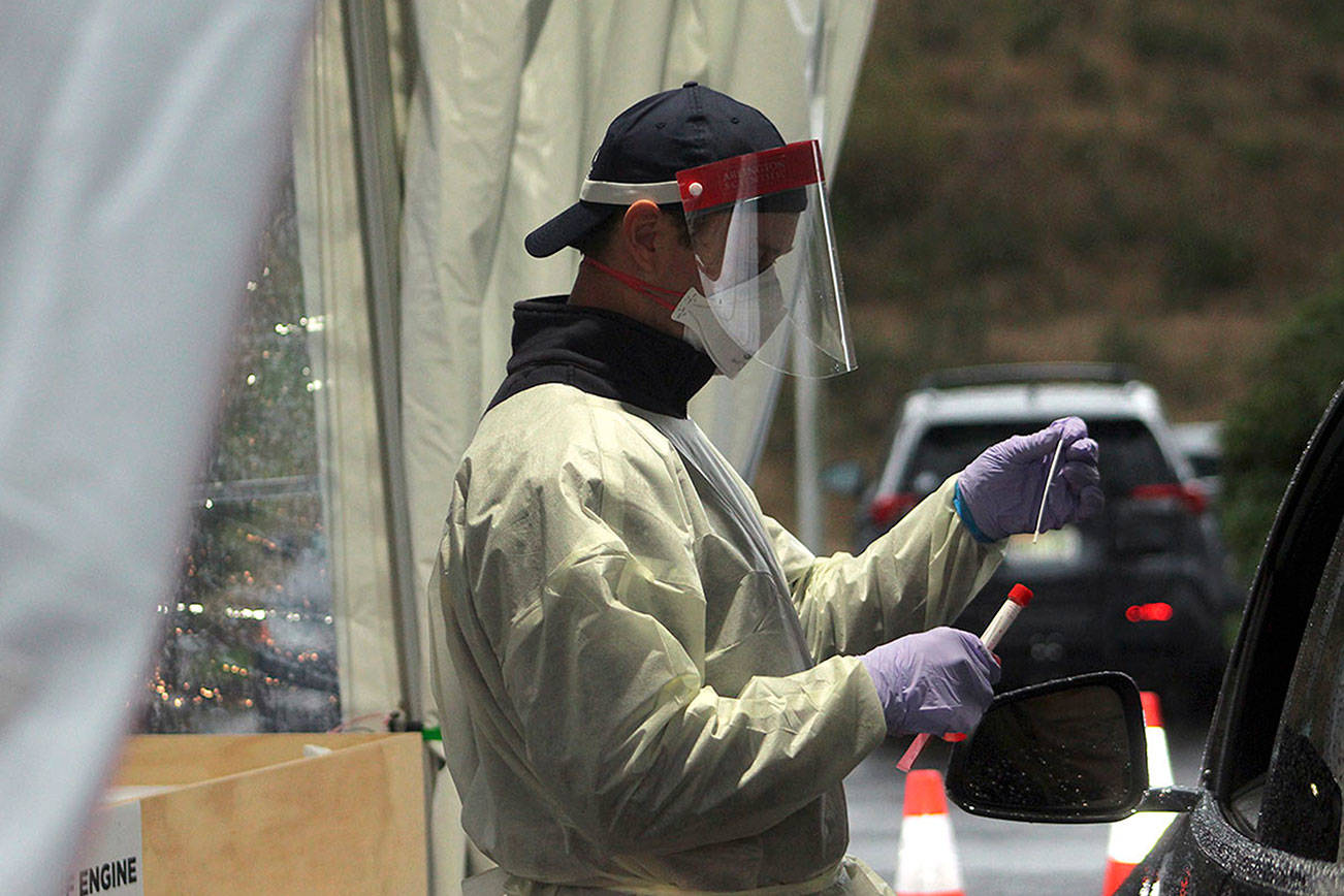 A South King Fire & Rescue firefighter places a used test swab into a secure COVID test vial on Nov. 18, 2020, at a Federal Way testing site. (Sound Publishing file photo)