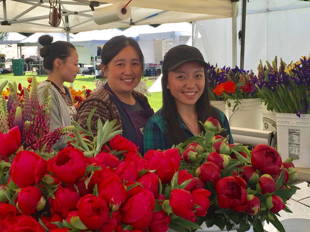 Regular floral vendors from Lia&rsquo;s Garden, of Snohomish, smile from a blaze of peonies. William Shaw/staff photo