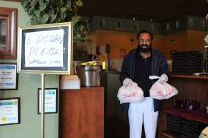 Kabal Gill, owner of East India Grill in Federal Way, wears gloves to hand over take-out orders at his restaurant on March 23. File photo